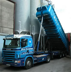 Historic blue McKnight Scania with a raised bulk tipper beside storage silos