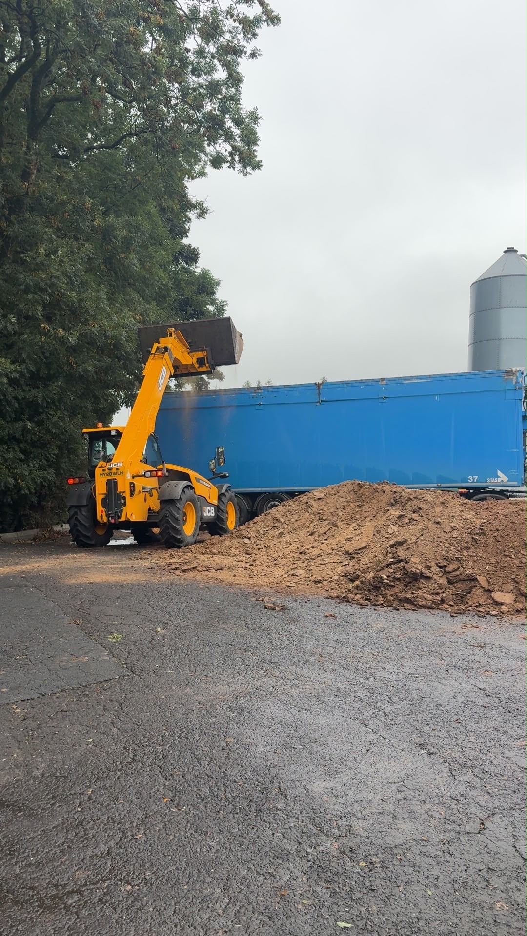 JCB loading chicken litter at a farm beside a blue McKnight bulk trailer